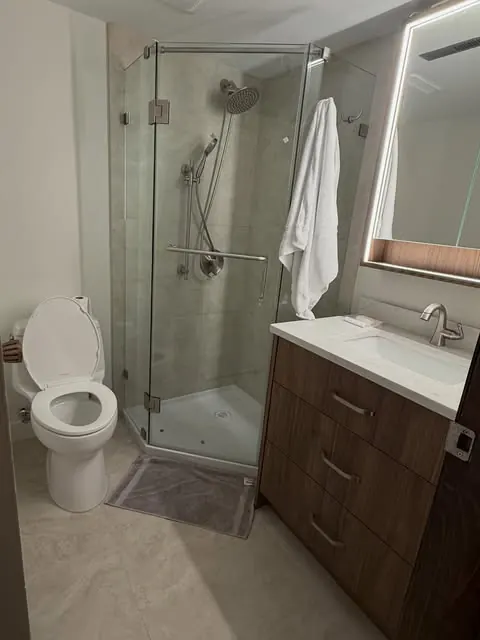 A finished bathroom renovation — walk-in glass shower, floating vanity, backlit mirror.