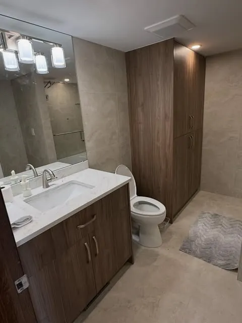 A finished bathroom renovation with a tall wood-tone vanity and lit mirror.