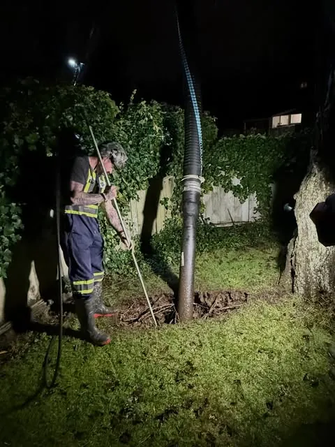 A Leak Busters technician clearing a line after dark, work light in hand.