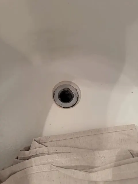 A drain opening exposed mid-repair in a bathtub, fixtures removed to trace where water is actually getting in.