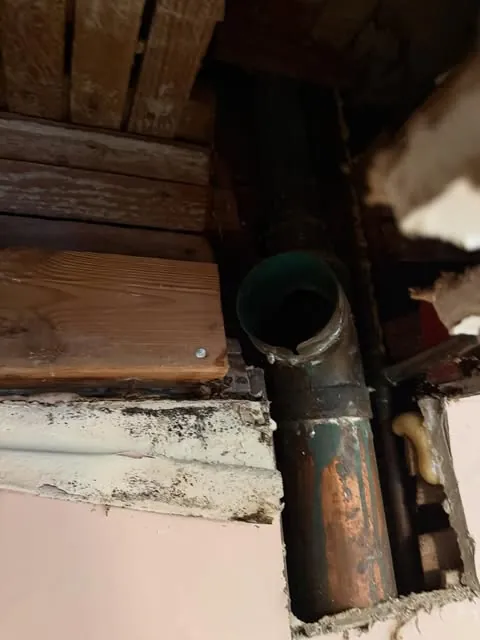 An open wall cavity mid-repair — copper supply line and a fresh fitting exposed between the studs, warm work light.