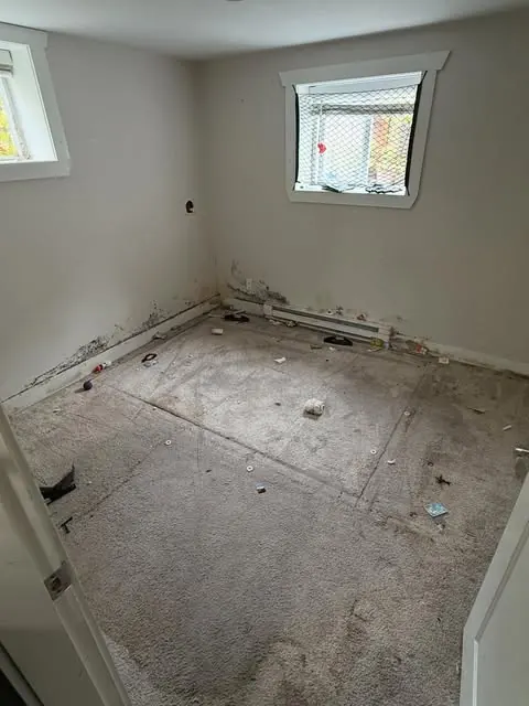 A room with water damage — carpet lifted, baseboard staining, drywall cut back for drying.